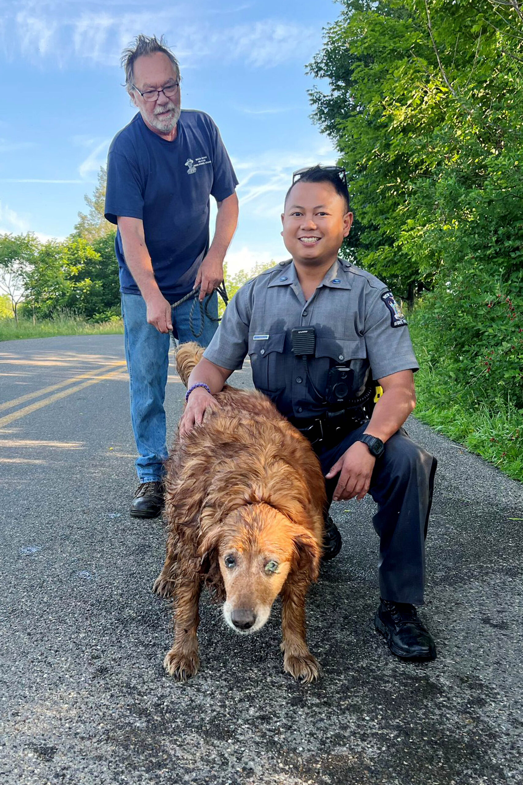 In this image provided by the New York State Police, Trooper Jimmy Rasaphone, right, poses for a photo with 13-year-old golden retriever Lilah, and her owner Rudy Fuehrer, after the trooper rescued her from a culvert pipe in Conklin, NY., on Sunday, June 26, 2022. Rasaphone grabbed a rope and crawled about 15 feet into the pipe, got to the dog and put her collar on her, and pulled the dog to safety with Fuehrer's help. (New York State Police via AP)