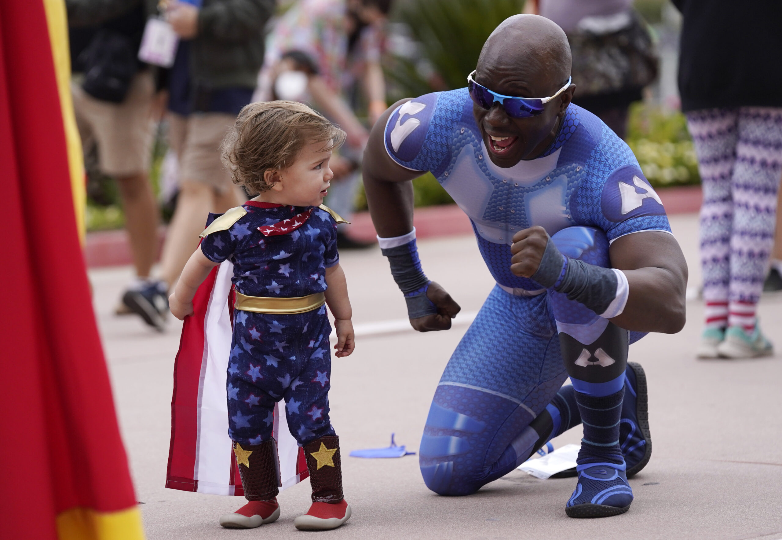Jay Acey, right, dressed as A-Train from the television series "The Boys," mingles with Maddox Cruz, 1, of Orange, Calif., outside Preview Night at the 2022 Comic-Con International at the San Diego Convention Center, Wednesday, July 20, 2022, in San Diego. (AP Photo/Chris Pizzello)