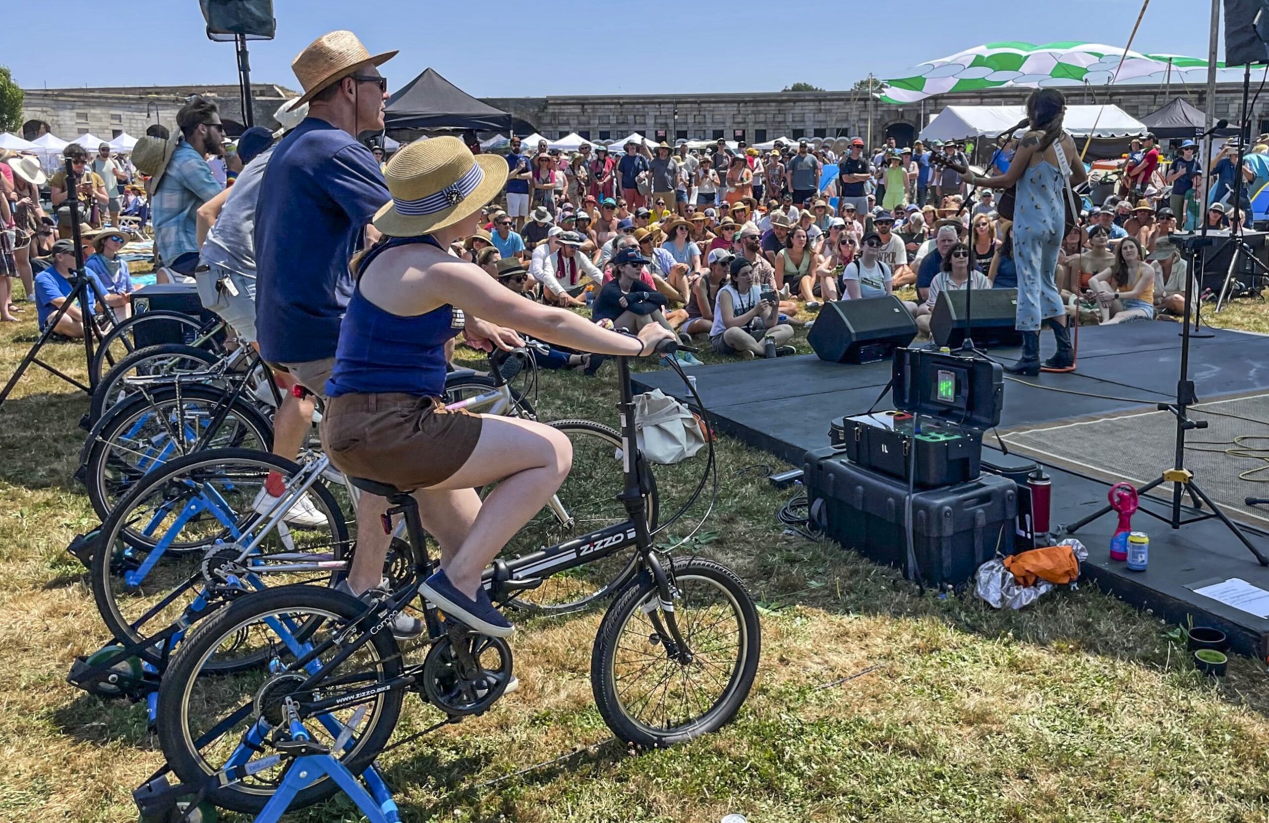 Madi Diaz, right, performs at the Newport Folk Festival's bike stage, powered in part by festivalgoers on stationary bicycles, left, Friday, July 22, 2022, in Newport, R.I. (AP Photo/Pat Eaton-Robb)