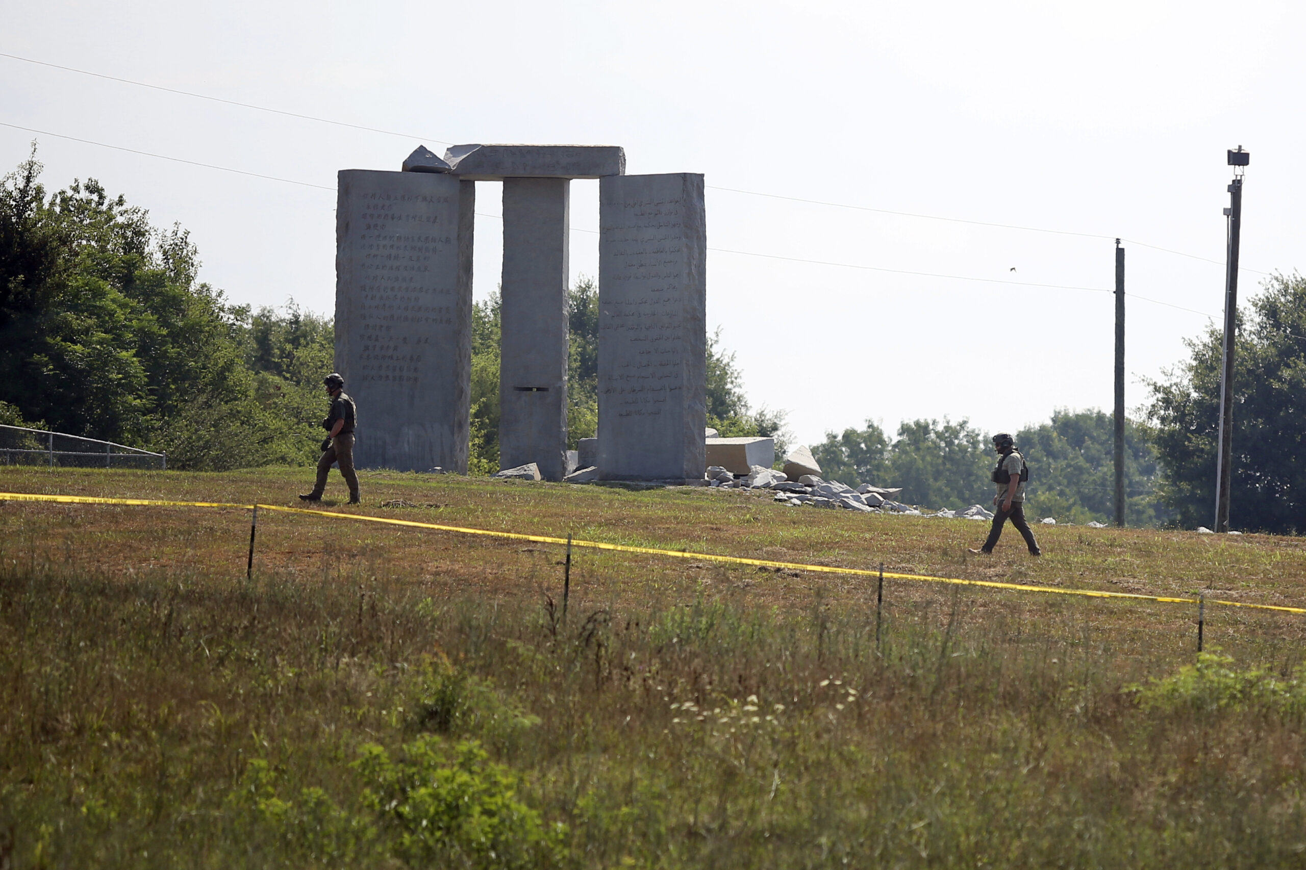 Law enforcement officials walk around the damaged Georgia Guidestones monument near Elberton, Ga., on Wednesday, July 6, 2022. The Georgia Bureau of Investigation said the monument, which some Christians regard as satanic, was damaged by an explosion before dawn. (Rose Scoggins/The Elberton Star via AP)