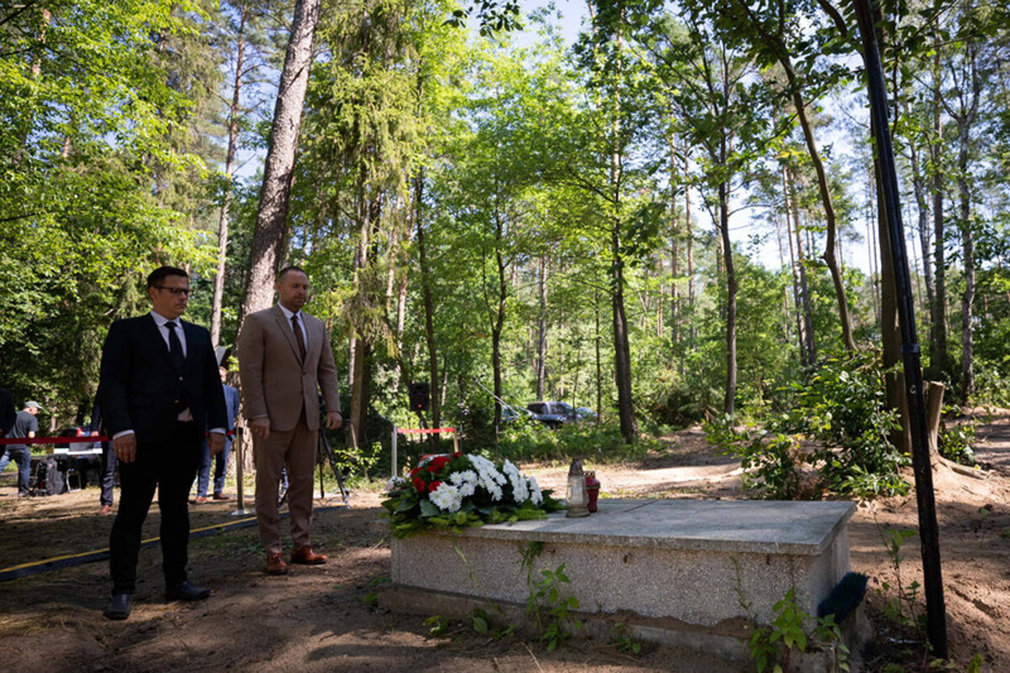 Karol Nawrocki, right, head of the Institute of National Remembrance (IPN), stands in front of a grave as he meets the media near Działdowo, Poland, Wednesday, July 13, 2022. Special investigators in Poland say they have found mass graves containing the ashes of at least 8,000 Poles slain by Nazi Germans during World War II in forest executions. The occupying Nazis tried to hide the killings by incinerating the bodies and planting trees on the burial pits. (Mikolaj Bujak/Institute of National Remembrance via AP)