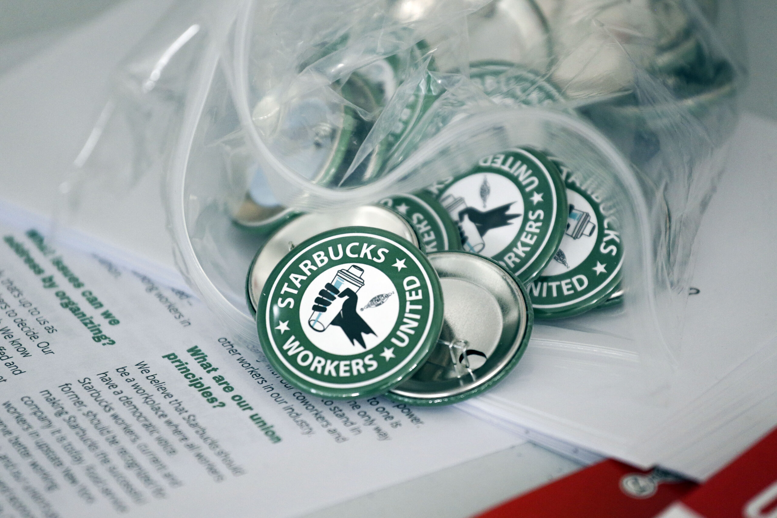 FILE — Pro-union pins sit on a table during a watch party for Starbucks' employees union election, Dec. 9, 2021, in Buffalo, N.Y. Starbucks is asking the National Labor Relations Board to temporarily suspend all union elections at its U.S. stores in response to allegations of improper coordination between regional NLRB officials and the union. (AP Photo/Joshua Bessex, File)