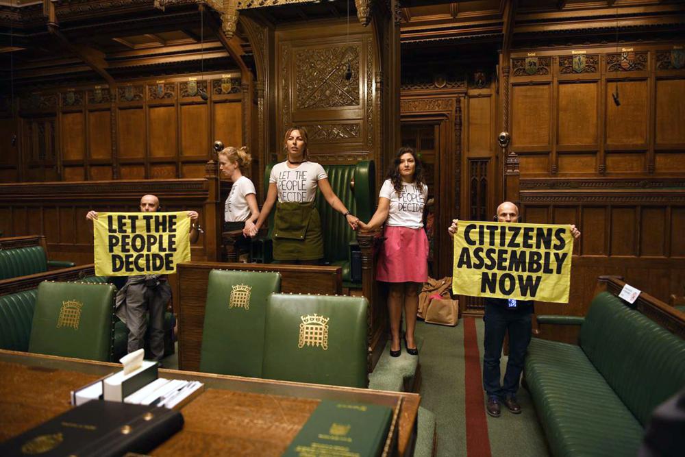 Extinction Rebellion activists stage a protest at the House of Commons chamber, British Parliament, in London, Friday Sept. 2, 2022. The environmental activist group Extinction Rebellion said Friday its supporters have superglued themselves to one another in a chain around the chair used by the speaker in the House of Commons chamber. A photo posted on Twitter showed three activists hand-in-hand in front of the seat while two other members held up signs. One sign read “Let the people decide” and the other noted “Citizens’ assembly now.″ (Extinction Rebellion UK via AP)