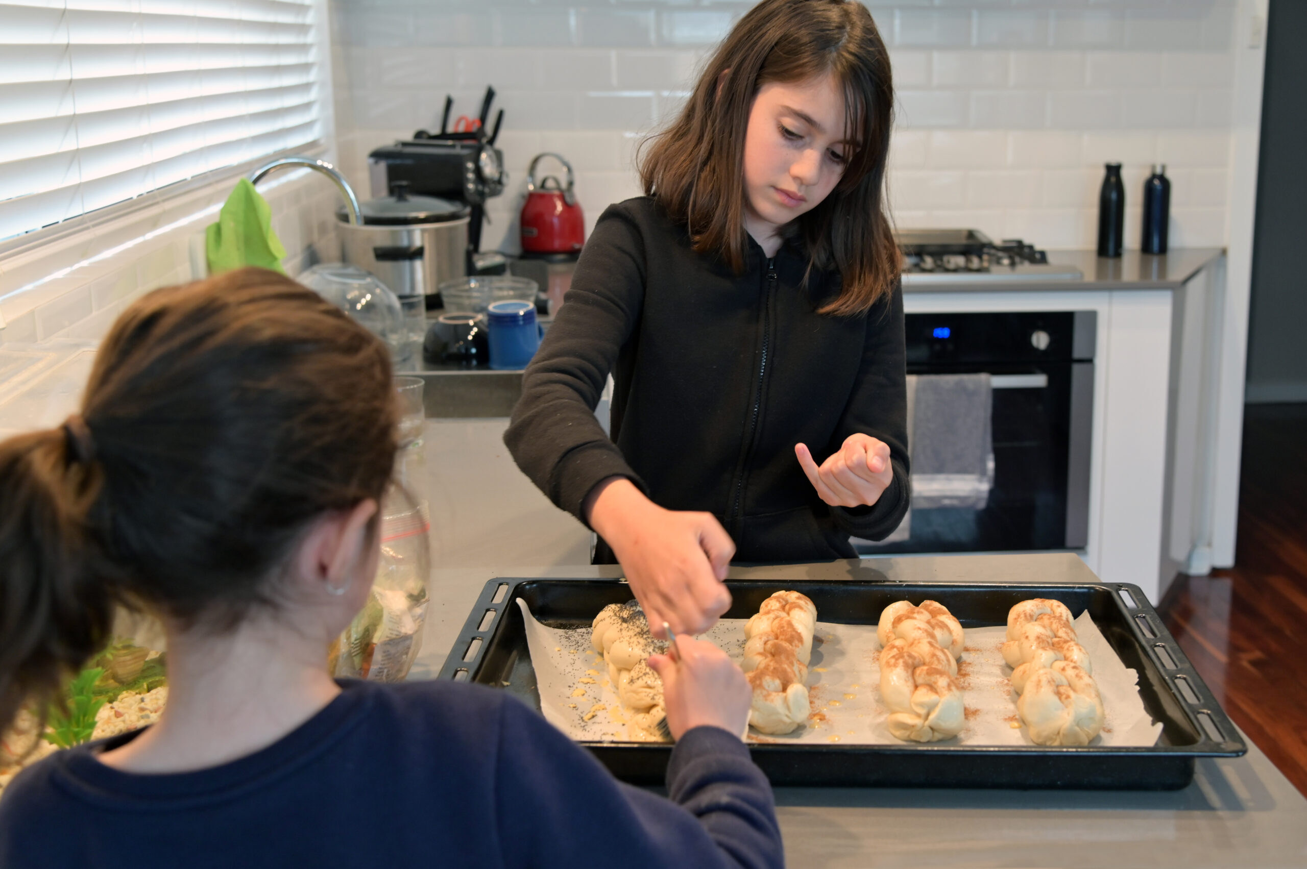 Two young Jewish girls (females age 07 and 11) baking challah bread in home kitchen for Sabbath Jewish holiday dinner.